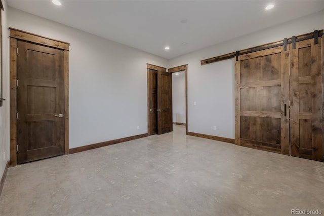 unfurnished bedroom with baseboards, concrete floors, and a barn door