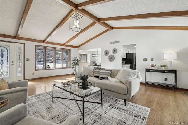 living room with light wood-type flooring, lofted ceiling with beams, a textured ceiling, and an inviting chandelier