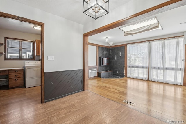 unfurnished living room with a wall mounted AC, washer / clothes dryer, and light hardwood / wood-style flooring