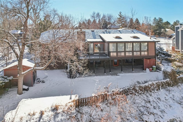 snow covered back of property with a sunroom and a deck