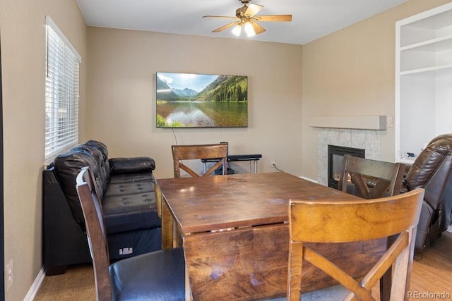 dining space with ceiling fan, a tile fireplace, and wood-type flooring