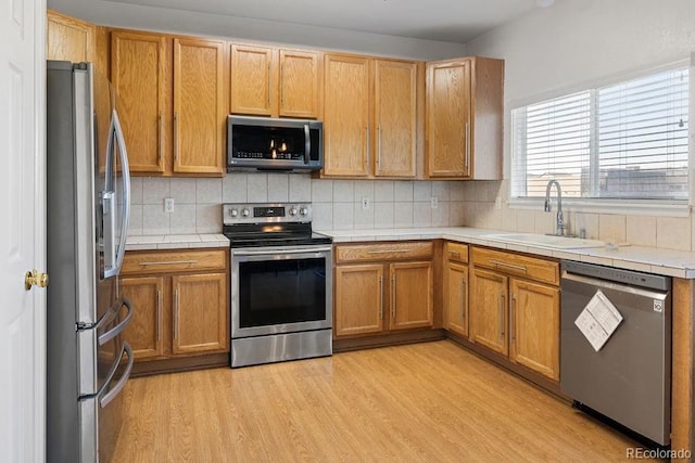 kitchen featuring stainless steel appliances, backsplash, sink, and light hardwood / wood-style flooring