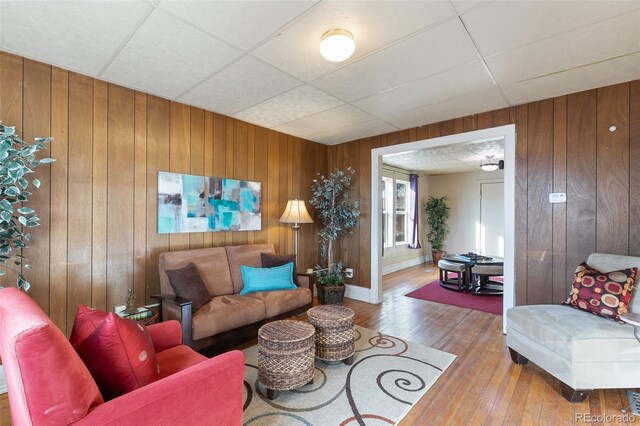 living room featuring wood walls, a drop ceiling, and wood-type flooring