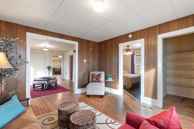 living room featuring built in shelves, ceiling fan, wooden walls, and light hardwood / wood-style flooring