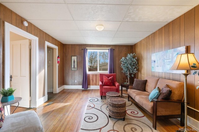 living room featuring light hardwood / wood-style floors, a drop ceiling, and wood walls