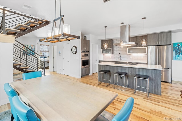 kitchen with stainless steel appliances, a center island, light wood finished floors, modern cabinets, and island exhaust hood