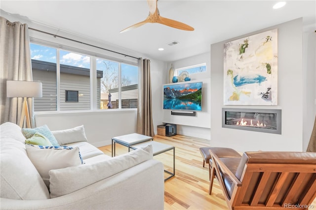 living room featuring recessed lighting, wood finished floors, visible vents, a ceiling fan, and a glass covered fireplace