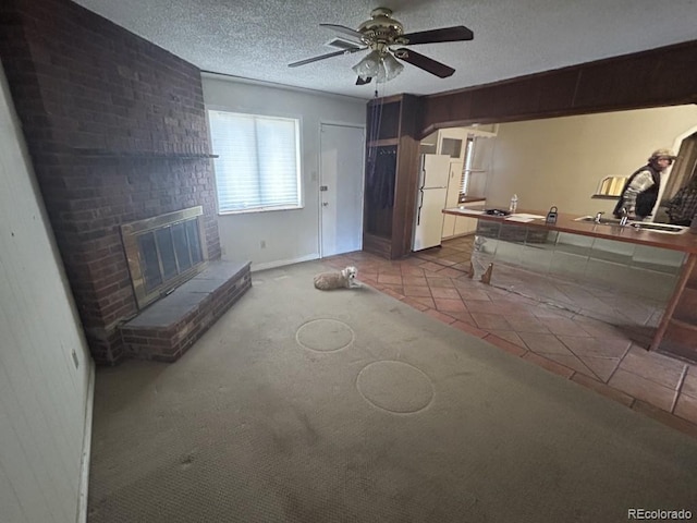 unfurnished living room with ceiling fan, a textured ceiling, light tile patterned floors, and a fireplace