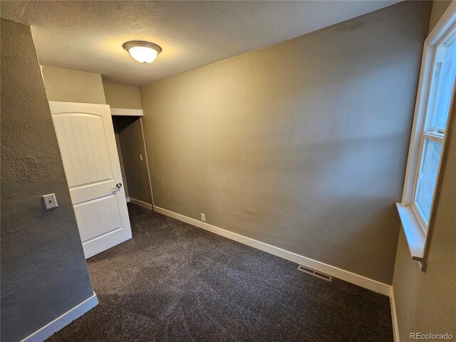 unfurnished room featuring dark colored carpet and a textured ceiling