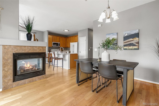 7130 Simms St Unit 206, Arvada, CO 80004 - dining room featuring a chandelier, light wood-type flooring, a tile fireplace, and baseboards