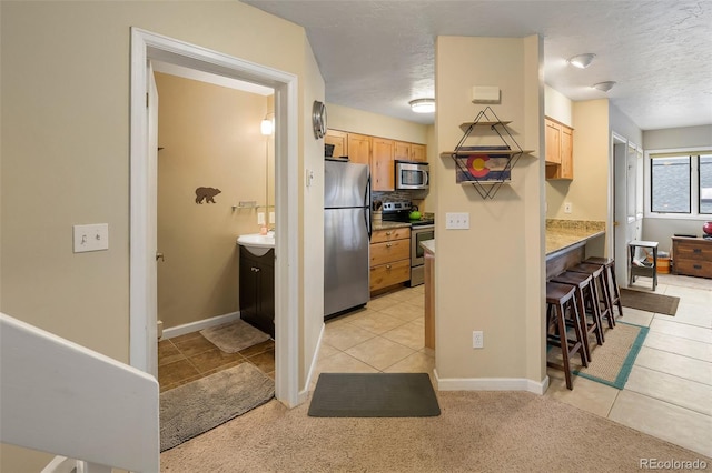 kitchen with light brown cabinetry, a breakfast bar area, light tile patterned floors, baseboards, and stainless steel appliances
