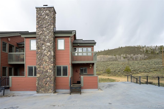 rear view of property with fence, a chimney, and a balcony