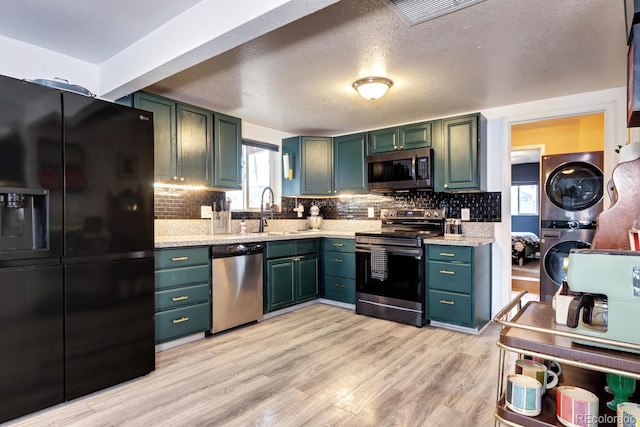 kitchen featuring light wood-type flooring, stacked washer / drying machine, stainless steel appliances, and decorative backsplash