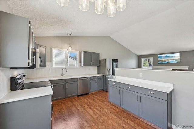kitchen with wood finished floors, a sink, appliances with stainless steel finishes, vaulted ceiling, and gray cabinetry