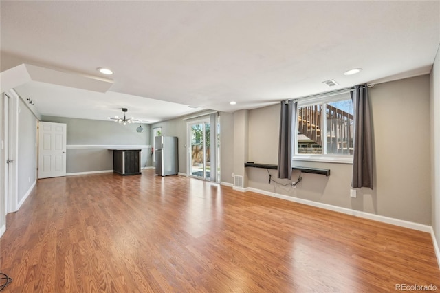 unfurnished living room with baseboards, an inviting chandelier, wood finished floors, and visible vents