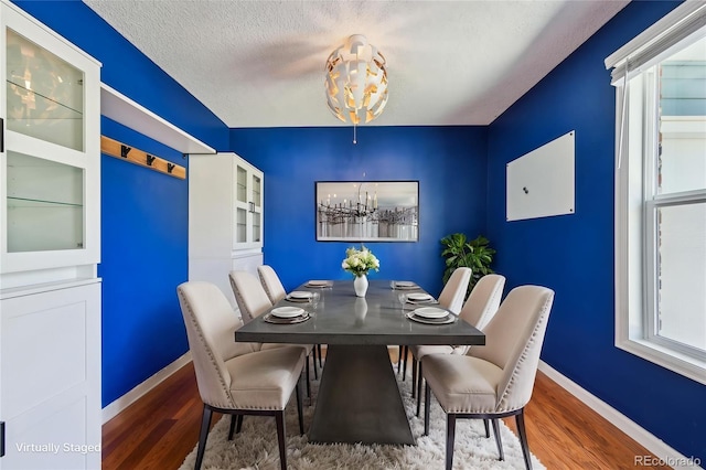 dining room featuring baseboards, a textured ceiling, wood finished floors, and a notable chandelier