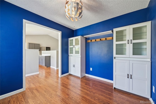 spare room with baseboards, a textured ceiling, a chandelier, and wood finished floors