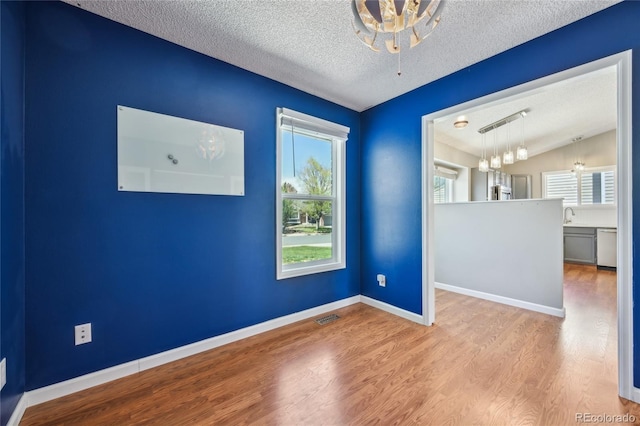 unfurnished room with a textured ceiling, visible vents, a notable chandelier, wood finished floors, and lofted ceiling