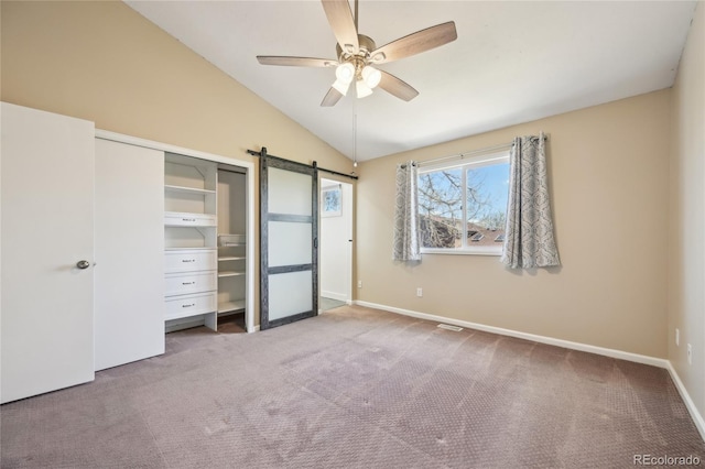 unfurnished bedroom with baseboards, vaulted ceiling, a barn door, and carpet