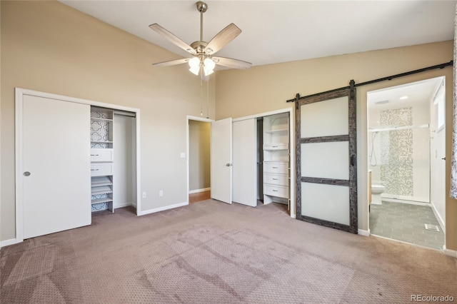 unfurnished bedroom featuring carpet flooring, connected bathroom, a barn door, multiple closets, and baseboards