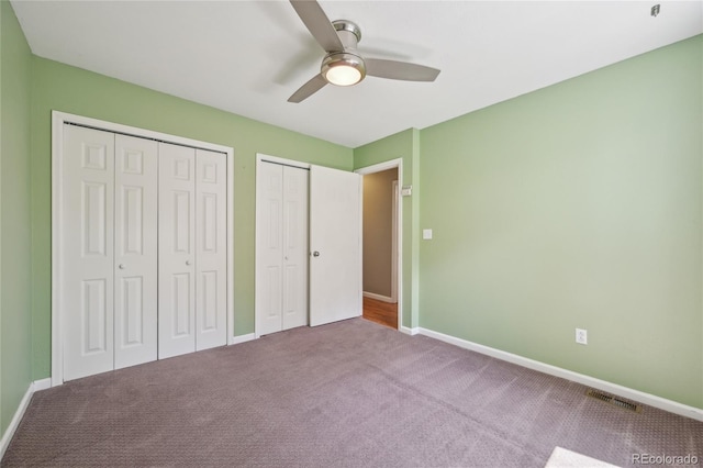 unfurnished bedroom with two closets, carpet flooring, visible vents, and baseboards