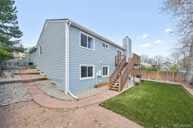 rear view of property featuring a chimney, a lawn, a deck, fence, and stairs