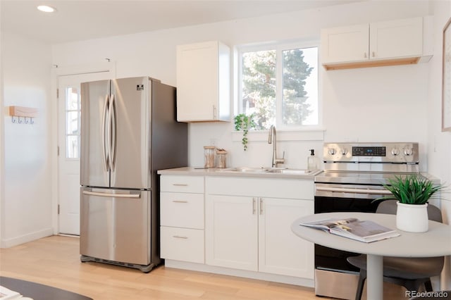 kitchen with light wood finished floors, stainless steel appliances, light countertops, white cabinets, and a sink