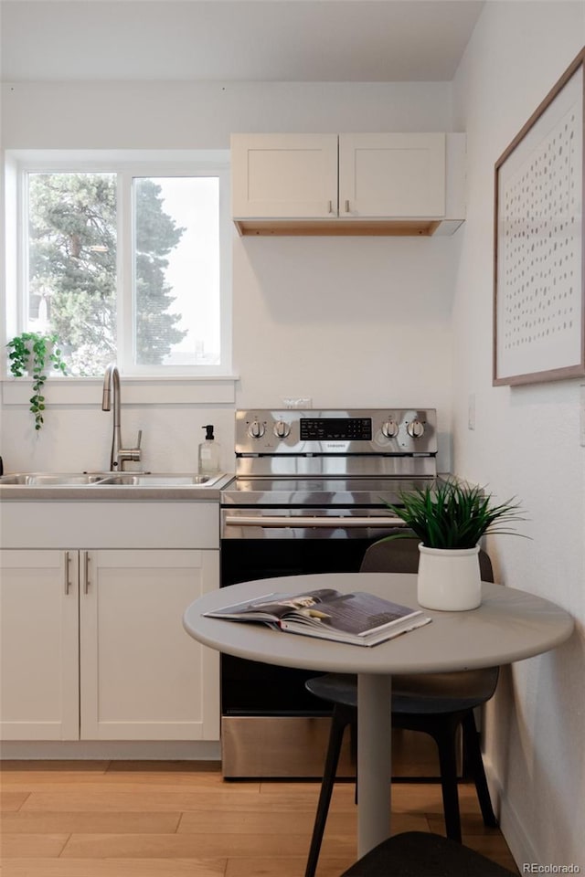 kitchen featuring light wood finished floors, light countertops, electric range, white cabinets, and a sink