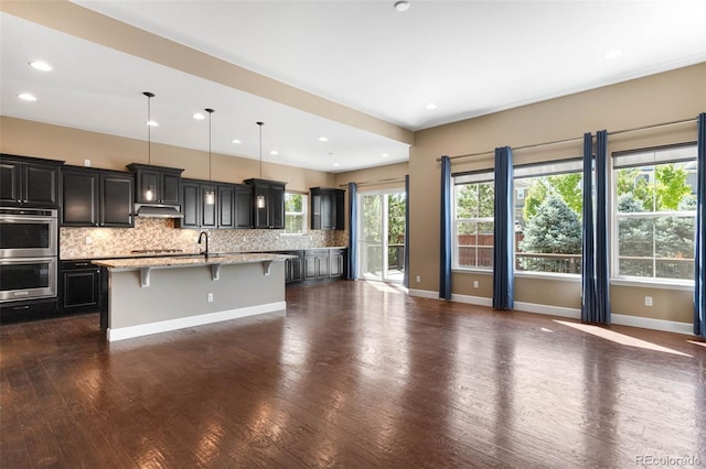 10122 Des Moines St, Parker, CO 80134 - kitchen with appliances with stainless steel finishes, a breakfast bar area, tasteful backsplash, an island with sink, and dark wood-style floors