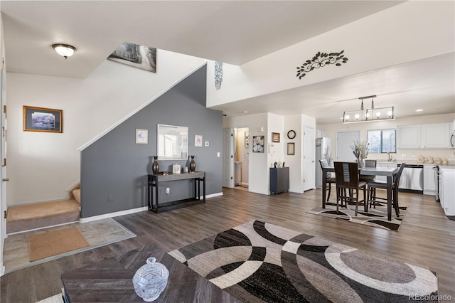 living area featuring baseboards, stairway, a chandelier, and dark wood-type flooring