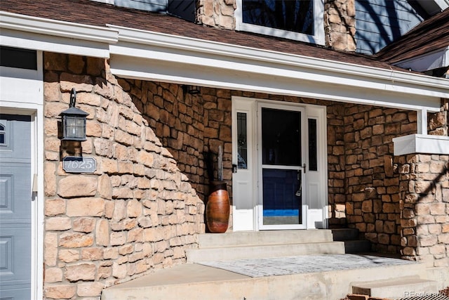 view of exterior entry with a garage, stone siding, and a shingled roof