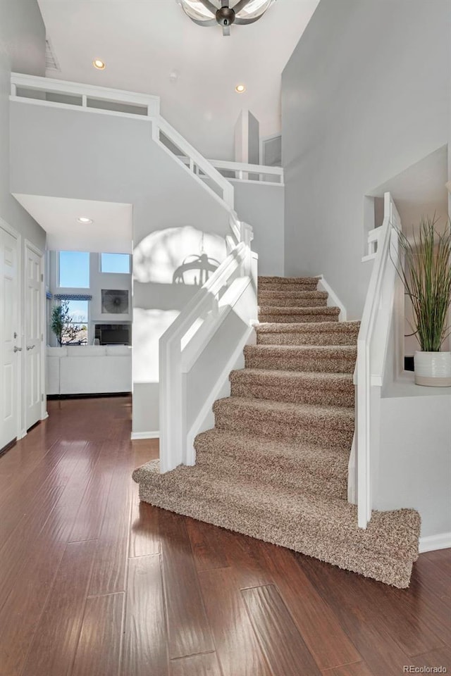 stairway with a towering ceiling, wood finished floors, and recessed lighting