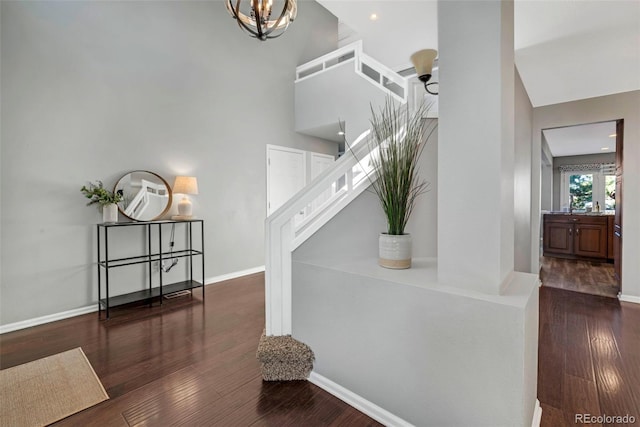 stairs with a chandelier, a high ceiling, wood finished floors, and baseboards