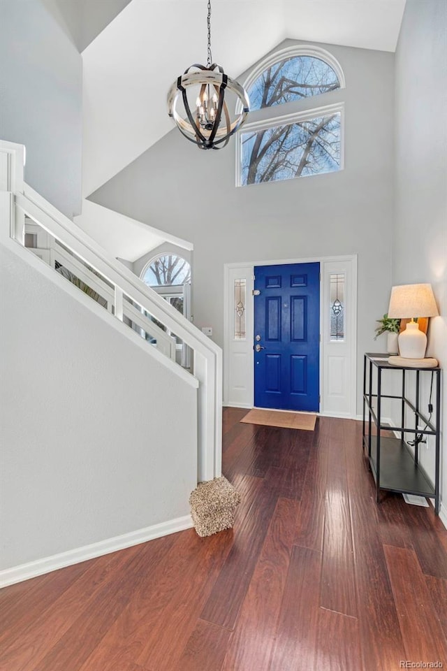 entrance foyer with high vaulted ceiling, wood finished floors, baseboards, stairs, and an inviting chandelier