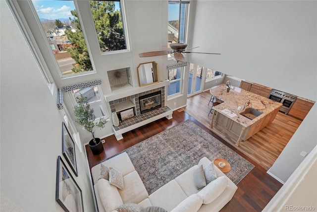 living area with a wealth of natural light, a tiled fireplace, and wood finished floors