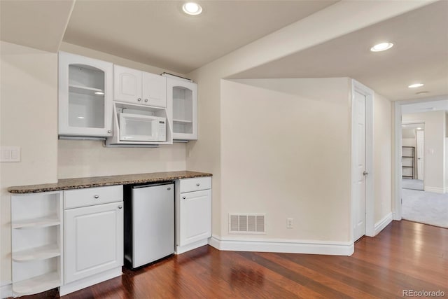 kitchen with dark stone counters, white cabinets, visible vents, and fridge