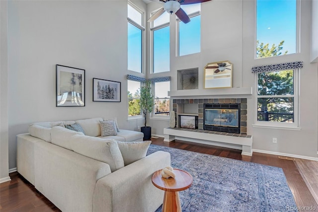 living room with a high ceiling, a ceiling fan, a glass covered fireplace, wood finished floors, and baseboards