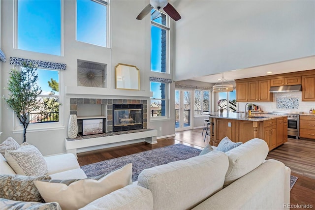 living room featuring dark wood-style floors, ceiling fan, a fireplace, and baseboards