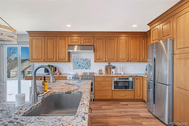 kitchen with light stone counters, tasteful backsplash, appliances with stainless steel finishes, a sink, and under cabinet range hood