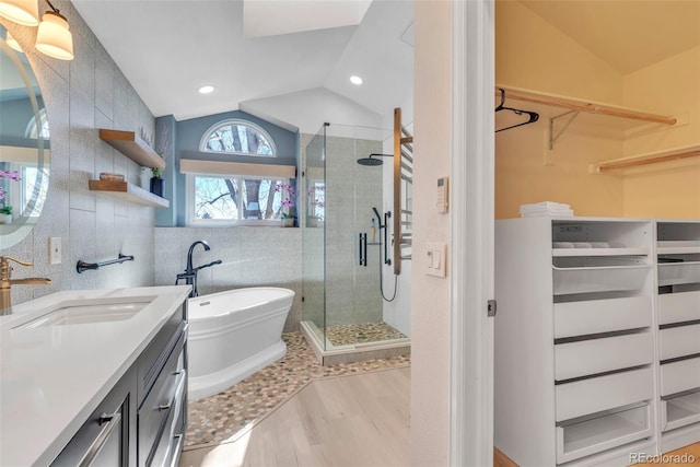 bathroom with a stall shower, vaulted ceiling, tile walls, and vanity