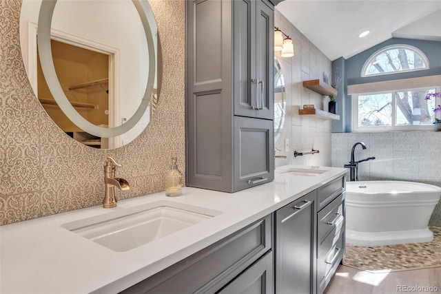 full bath with a freestanding bath, tile walls, vaulted ceiling, and a sink