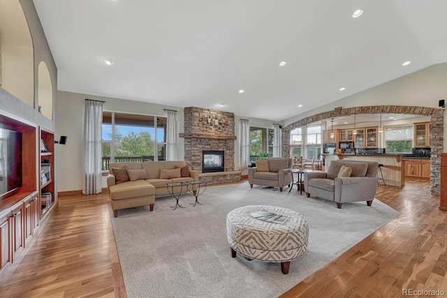 living area with lofted ceiling, a stone fireplace, light wood-type flooring, and recessed lighting