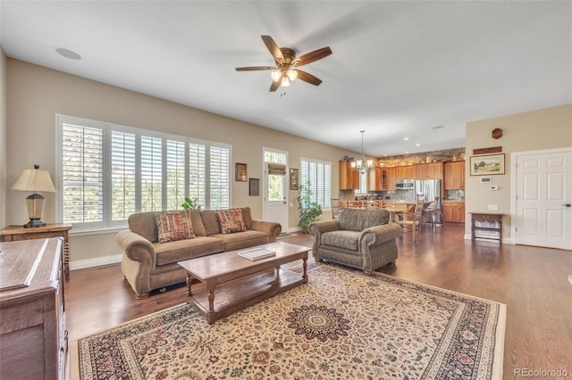 living area with baseboards, dark wood finished floors, and ceiling fan with notable chandelier