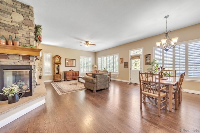 living room featuring a stone fireplace, ceiling fan with notable chandelier, baseboards, and wood finished floors