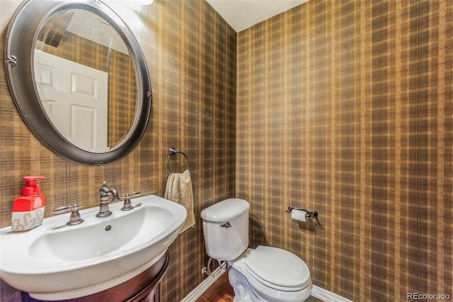 half bathroom with wallpapered walls, toilet, baseboards, and a sink