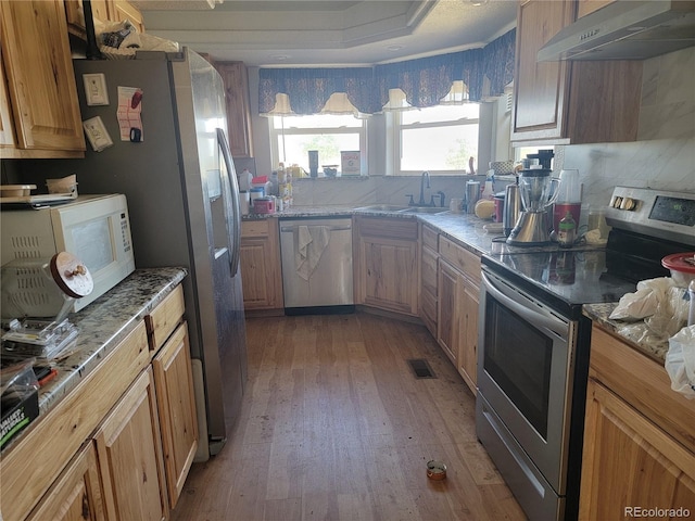 71777 E County Road 10, Byers, CO 80103 - kitchen featuring appliances with stainless steel finishes, exhaust hood, light wood-style flooring, stone counters, and brown cabinetry