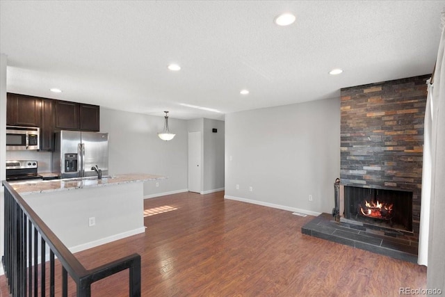 kitchen featuring a tile fireplace, appliances with stainless steel finishes, decorative light fixtures, dark hardwood / wood-style flooring, and dark brown cabinetry