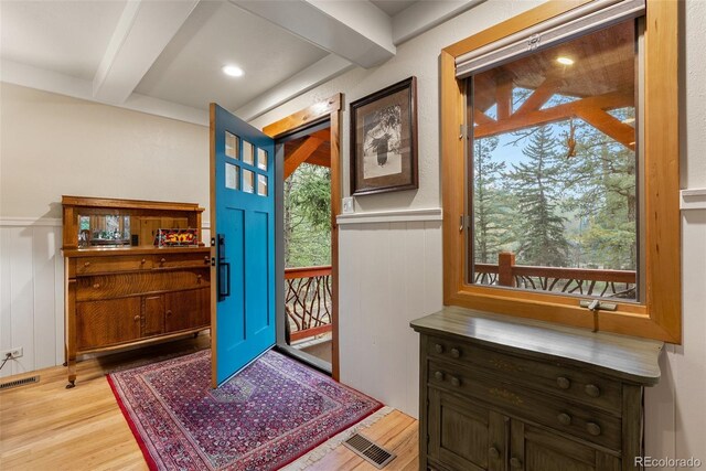 foyer with beam ceiling, wood finished floors, a wainscoted wall, and a decorative wall