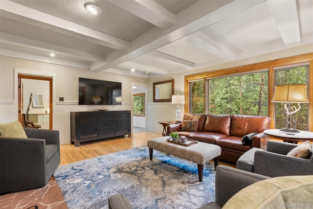 living room featuring beamed ceiling, light wood-style flooring, and a wainscoted wall