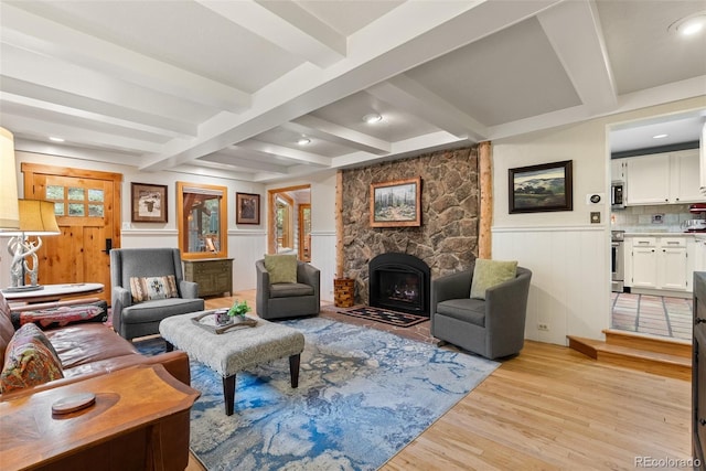 living area featuring light wood finished floors, beam ceiling, wainscoting, and a fireplace